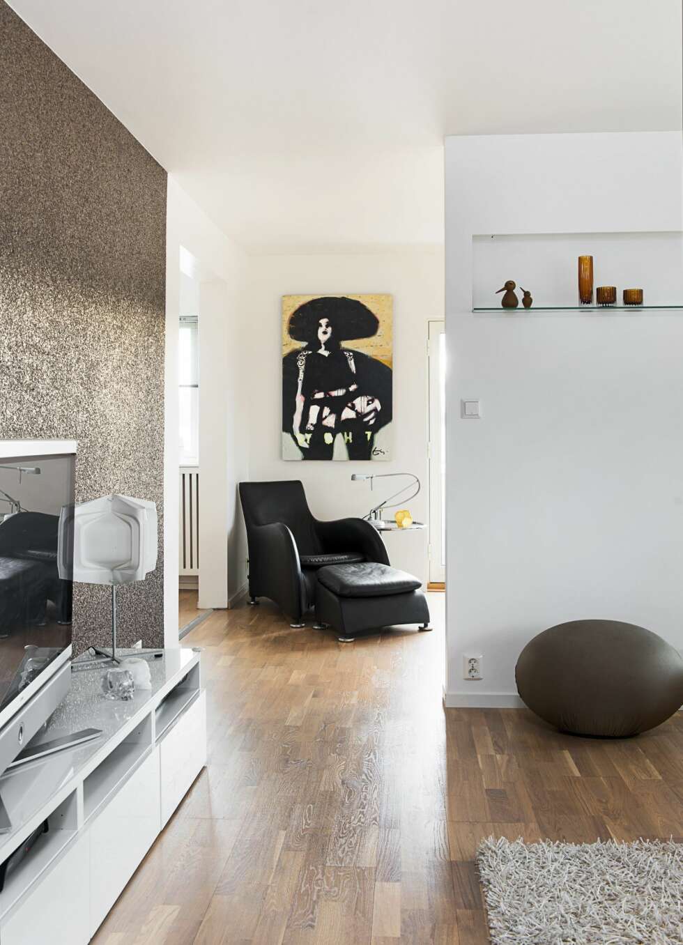 SKILLEVEGG: En lettvegg ble satt opp midt i stuen. Den har åpning på begge sider slik at det fremdeles kommer lys inn fra vinduene. Interiørarkitekten tegnet en hylle innebygget i skilleveggen, der får fine ting stå fremme. Det glitrende tapetet AKA 3004 er fra Omexco. Stolen Montis, designet av Gerard van den Berg, står i avslapningskroken, bildet er av Espen Eiborg. Bak lettveggen har beboerne etablert trenings- og arbeidsplass. Rund puff fra Cerutti Balleri. SKILLEVEGG: En lettvegg ble satt opp midt i stuen. Den har åpning på begge sider slik at det fremdeles kommer lys inn fra vinduene. Interiørarkitekten tegnet en hylle innebygget i skilleveggen, der får fine ting stå fremme. Det glitrende tapetet AKA 3004 er fra Omexco. Stolen Montis, designet av Gerard van den Berg, står i avslapningskroken, bildet er av Espen Eiborg. Bak lettveggen har beboerne etablert trenings- og arbeidsplass. Rund puff fra Cerutti Balleri.