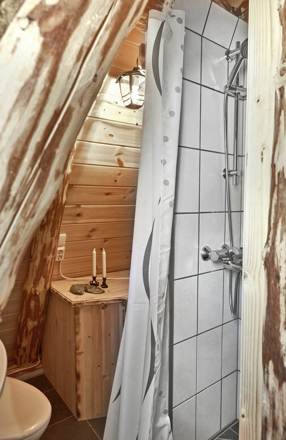 EFFEKTIV PLANLØSNING: Både dusj, toalett og vaskeservant har fått plass under skråveggene. Badet er adskilt fra resten av rommet ved hjelp av én bærende søyle som kan skimtes innerst på kjøkkenet. I tillegg er to «falske» søyler satt opp i samme tømmerstokkstil, og danner de to andre hjørnene på det som er dusjhjørnet. Disse to søylene er altså ikke nødvendige for konstruksjonen. FOTO: Sveinung Bråthen EFFEKTIV PLANLØSNING: Både dusj, toalett og vaskeservant har fått plass under skråveggene. Badet er adskilt fra resten av rommet ved hjelp av én bærende søyle som kan skimtes innerst på kjøkkenet. I tillegg er to «falske» søyler satt opp i samme tømmerstokkstil, og danner de to andre hjørnene på det som er dusjhjørnet. Disse to søylene er altså ikke nødvendige for konstruksjonen. FOTO: Sveinung Bråthen