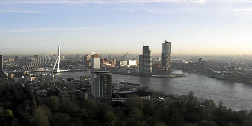 MELLOM TÅRNENE: Hotel New York ligger som en svart, liten prikk mellom de høyeste byggene ytterst på Kop van Zuid-landtungen, midt i Rotterdams havnebasseng. Dette er for tiden Europas travleste byggeplass. Til venstre byens nye landemerke, Erasmus-broen, populært kalt "Svanen" signert arkitekt Ben van Berkel. MELLOM TÅRNENE: Hotel New York ligger som en svart, liten prikk mellom de høyeste byggene ytterst på Kop van Zuid-landtungen, midt i Rotterdams havnebasseng. Dette er for tiden Europas travleste byggeplass. Til venstre byens nye landemerke, Erasmus-broen, populært kalt "Svanen" signert arkitekt Ben van Berkel.