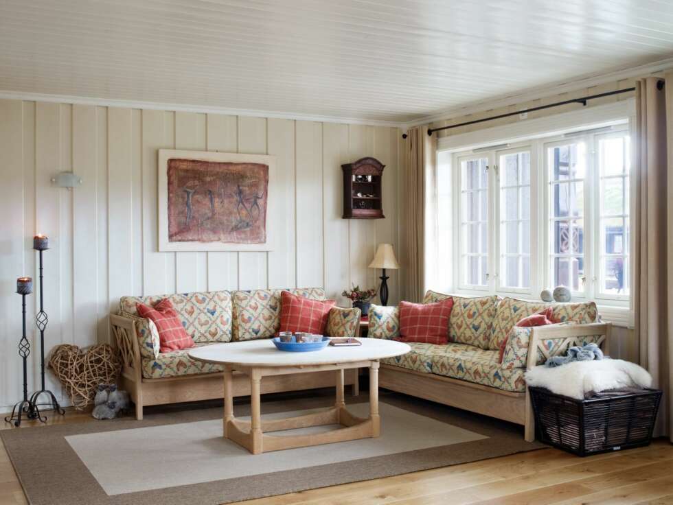 LANDLIG: Sofagruppen Skipper fra Tonning har en myk, beige grunntone og mønster med blå og røde haner. Bildet, som er kjøpt til hytta, er laget av kunstneren Christine Wyller. LANDLIG: Sofagruppen Skipper fra Tonning har en myk, beige grunntone og mønster med blå og røde haner. Bildet, som er kjøpt til hytta, er laget av kunstneren Christine Wyller.