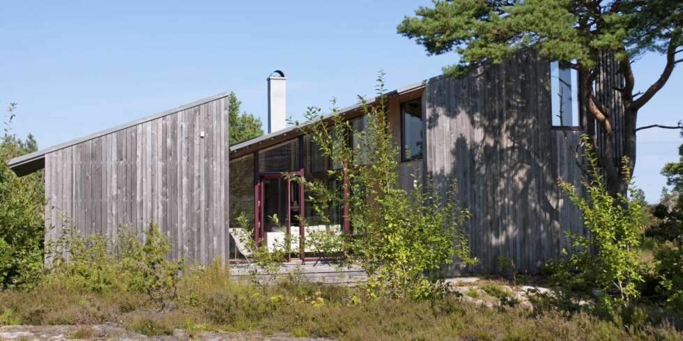 SKJERMET. Hytta på Tromøya er tegnet inn i terrenget. Den ligger godt skjermet blant furutrær og kratt. Ytterkledningen er i grånet osp. SKJERMET. Hytta på Tromøya er tegnet inn i terrenget. Den ligger godt skjermet blant furutrær og kratt. Ytterkledningen er i grånet osp.