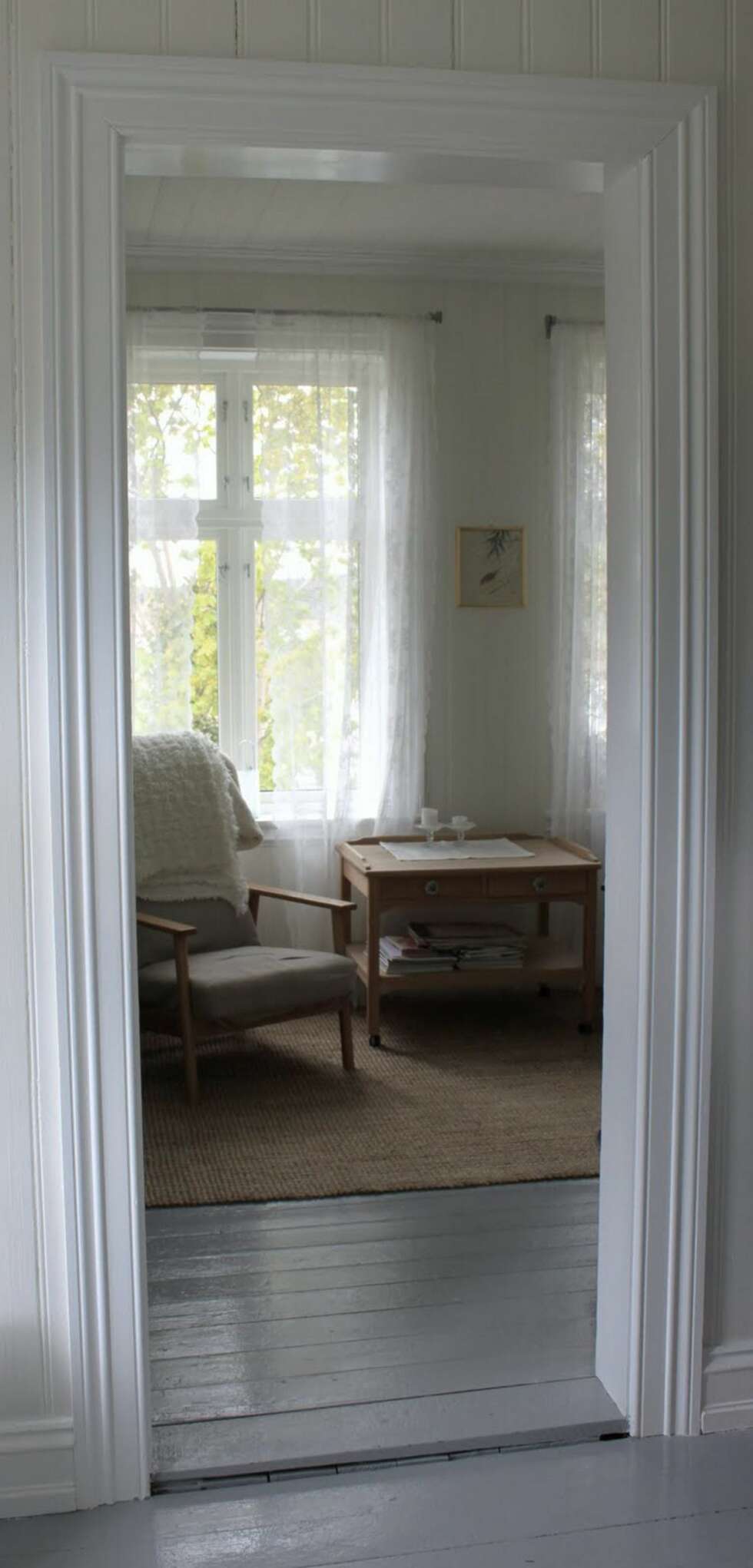 Fra gangen ser man inn i stuen. De gamle tregulvene er blitt malt grå. Fra gangen ser man inn i stuen. De gamle tregulvene er blitt malt grå.