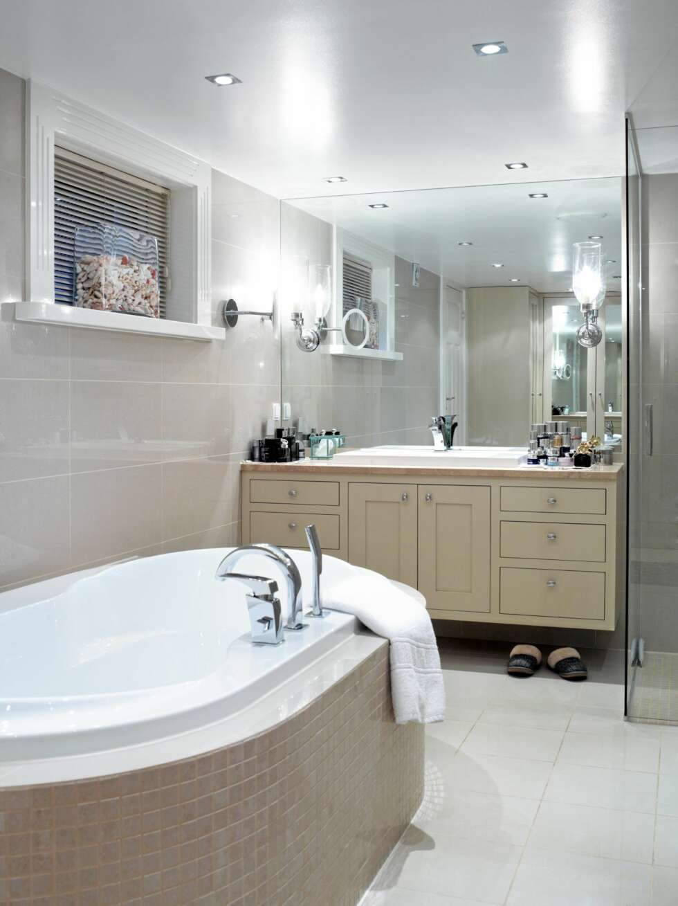 LYST BAD. Badet preges av duse farger, både på fliser og på baderomsmøblementet. Tak, vinduslister og gulvflisene er derimot holdt i hvitt. Det ovale badekaret er omringet av beige mosaikk, og i vinduskarmen står en glasskrukke med koraller fra Maldivene. LYST BAD. Badet preges av duse farger, både på fliser og på baderomsmøblementet. Tak, vinduslister og gulvflisene er derimot holdt i hvitt. Det ovale badekaret er omringet av beige mosaikk, og i vinduskarmen står en glasskrukke med koraller fra Maldivene.