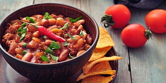 Chili Con Carne in bowl with tortilla chips on wooden background Chili Con Carne in bowl with tortilla chips on wooden background