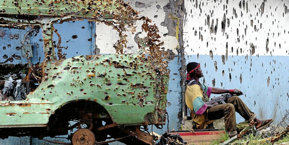 En opprørssoldat puster ut i et øyeblikks våpenhvile blant sønderskutte hus og kjøretøy, under borgerkrigen i Liberia i 2003. En opprørssoldat puster ut i et øyeblikks våpenhvile blant sønderskutte hus og kjøretøy, under borgerkrigen i Liberia i 2003.