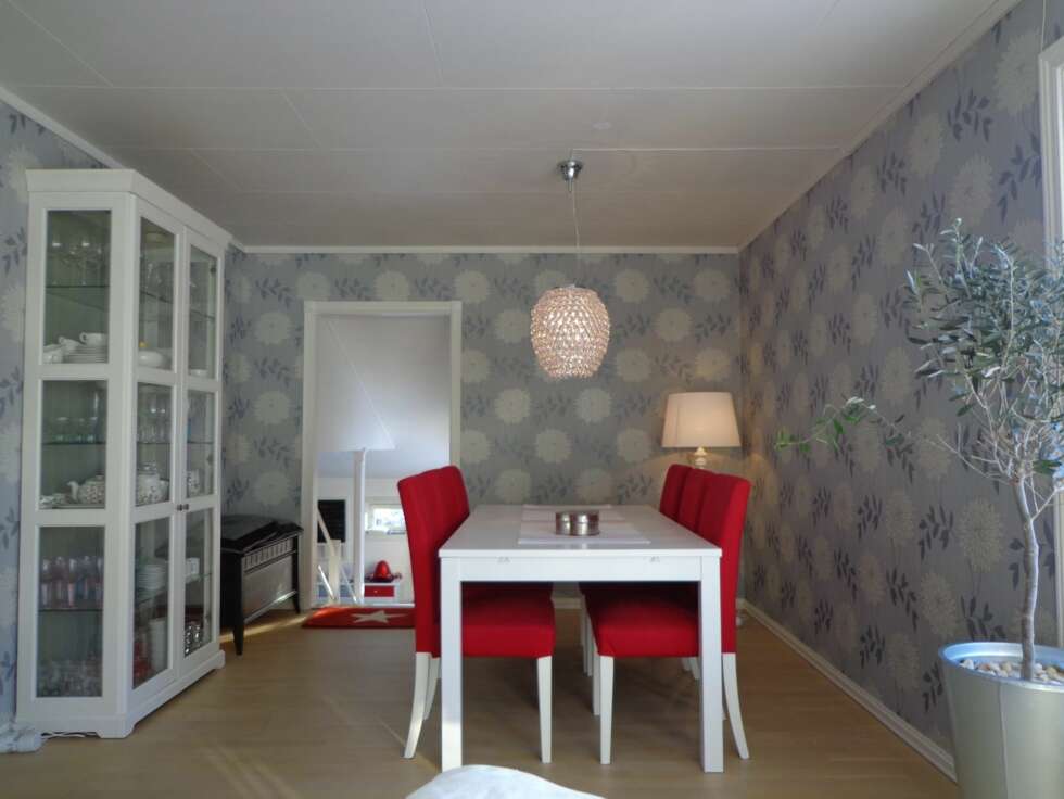 Spisestuedelen i stuen har fått blå tapet med blomstermotiv, mens det røde fra kjøkkenet går igjen i møbler og detaljer. Spisestuedelen i stuen har fått blå tapet med blomstermotiv, mens det røde fra kjøkkenet går igjen i møbler og detaljer.