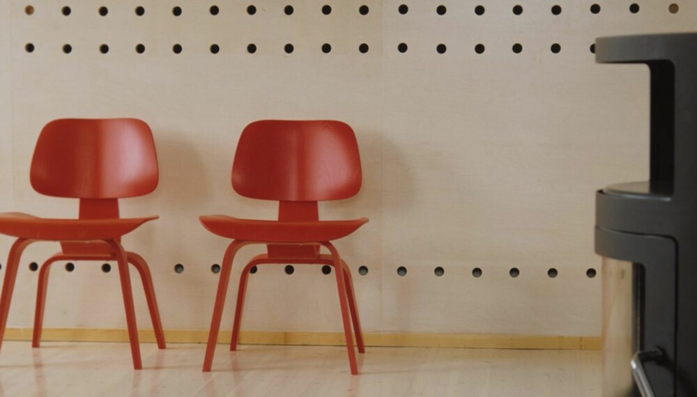 DESIGN I HØYSETET: Her ser du en snipp av  skillleveggen som deler leiligheten i Ullevål Hageby i to. Foran to røde Vitra finerstoler designet av Charles Eames. De matsjer dette rene, stramme interiøret perfekt.