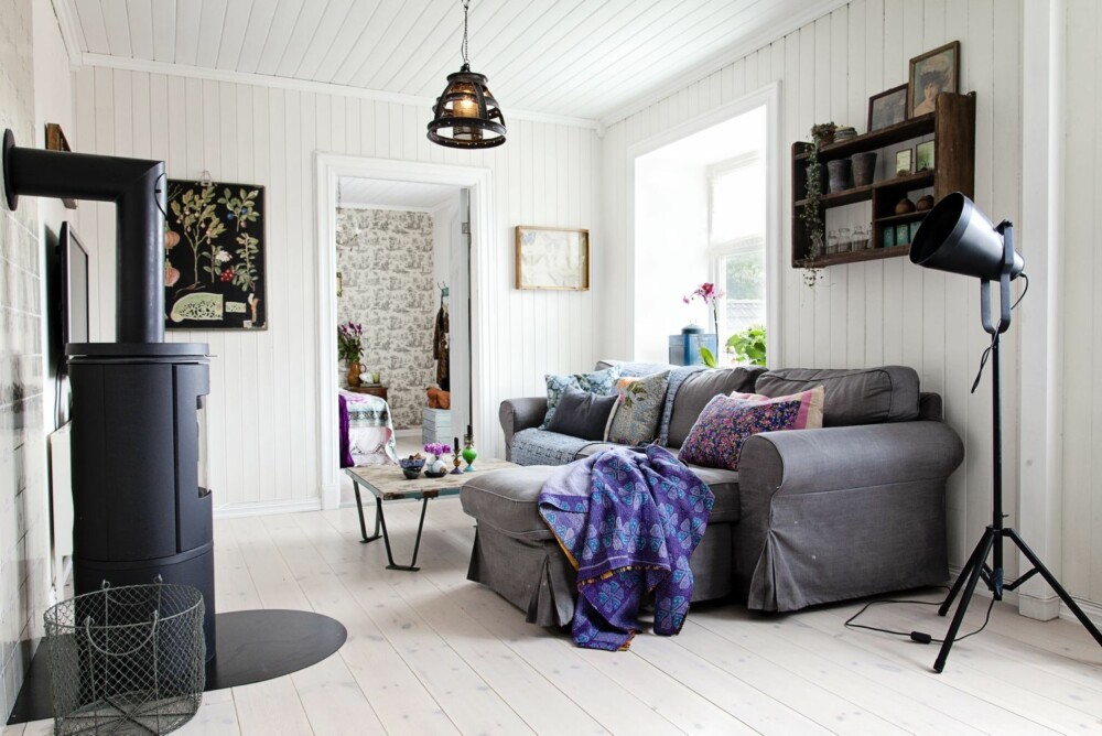 LUN STUE: Sofakroken er det innredet med myke tekstiler og puter. Den gamle trehyllen på veggen har Helene hatt med seg i mange år. Stålampen er fra Country Chic, taklampen fra Home & Cottage, stuebordet fra Nordahl, det lilla indiske tekstilet er fra Bloomingville. Vedovnen kommer fra ovnleverandøren Morsø.