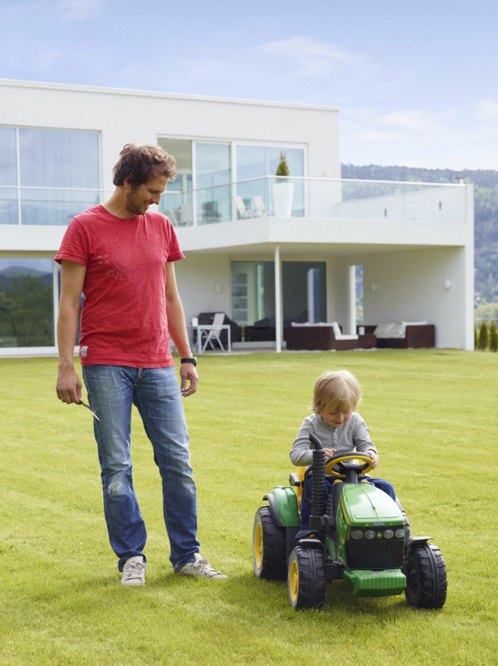 KAN SIN TRAKTOR: - Dette er en John Deere, sier Albert på traktoren. Han viser stor interesse for foreldrenes jobb. Her er han sammen med pappa Hans-Albert på plenen bak huset. Fra terrassen går man rett inn i stuen. Fra balkongen trer man inn i spisestue og kjøkken. Vinduer og skyvedører er i selvrensende glass, levert av tyske Schüco.