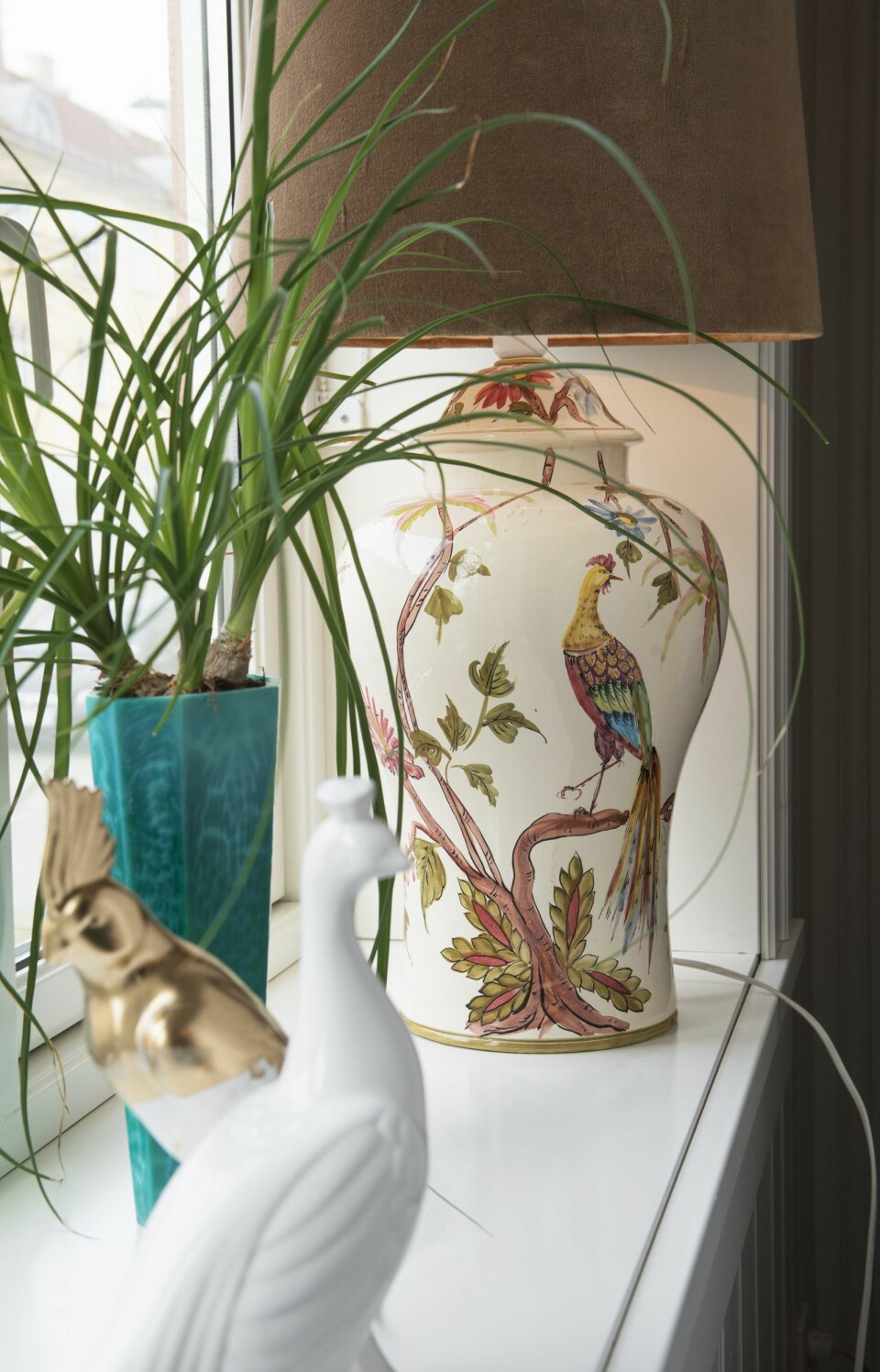 Brede vinduskarmer får liv av lamper, planter og nøye utvalgt nips. Påfugllampen er arvegods
fra Idas familie, vasen er et loppefunn, og fuglene er fra Skeidar, Ida har dyppet en av dem i gullmaling for å skape variasjon.