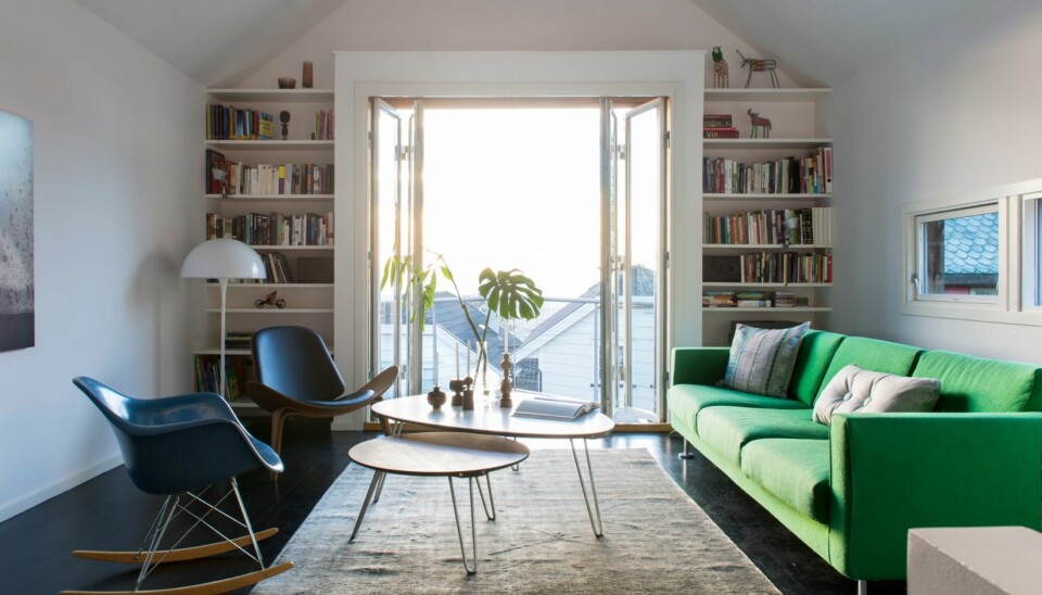 STEMNINGSFULLT: Stuen er i likhet med huset smalt og høyt. Rommet henvender seg mot balkongen i sør, mot lyset, og utsikten. Park Sofa og Eames Plastic Armchair fra Vitra. Sofabord, teppe og Shell Chair fra Verket interiør. Bokhyllene på hver side av foldedørene er tegnet av arkitekt Søren Sandved. Styling: Juni Hjartholm.