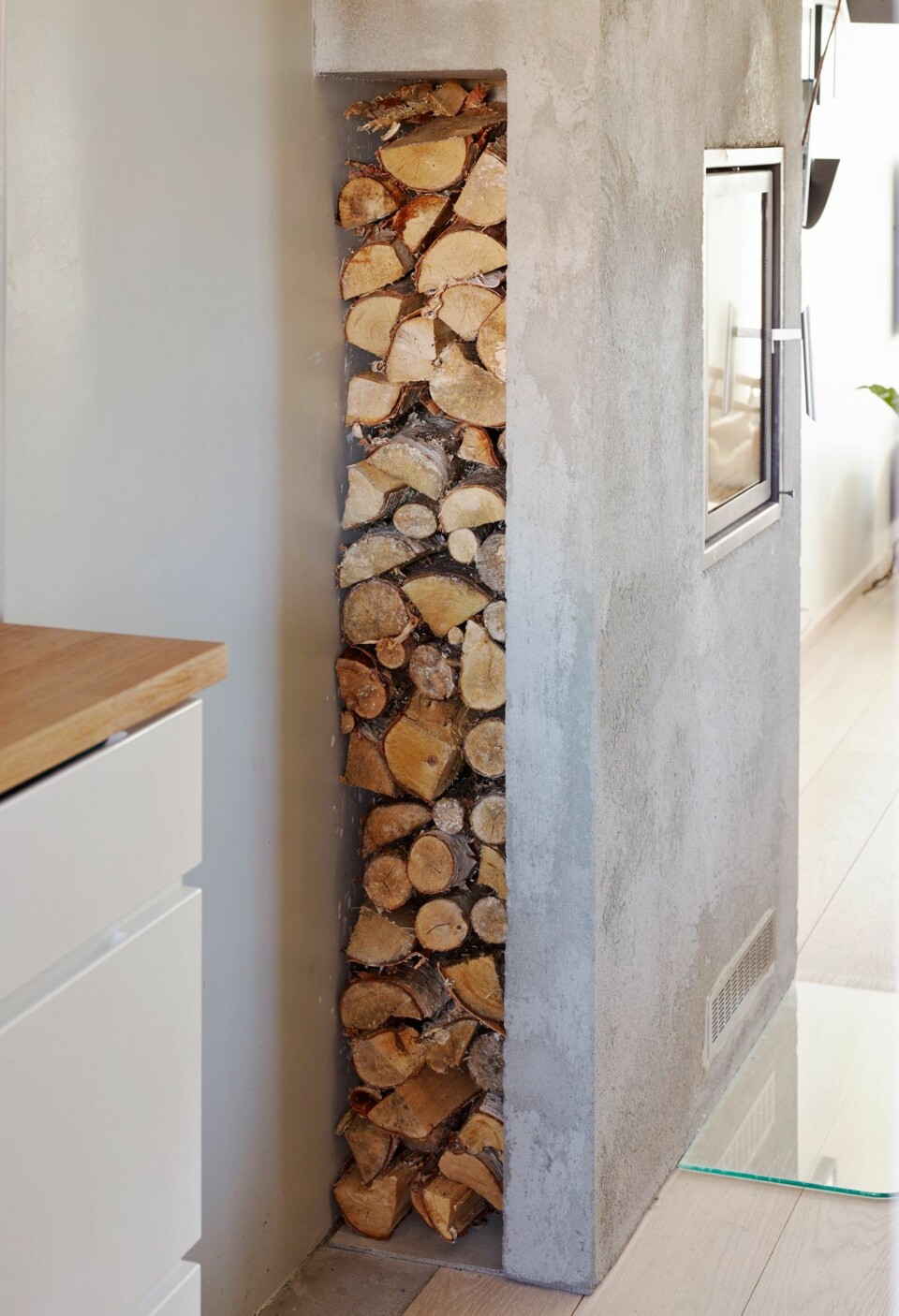 DEKORATIV OPPBEVARING: Mot kjøkkensiden ble det plass til oppbevaring av ved, praktisk og dekorativt. Veggen er dekket
med murpuss for et røffere uttrykk.