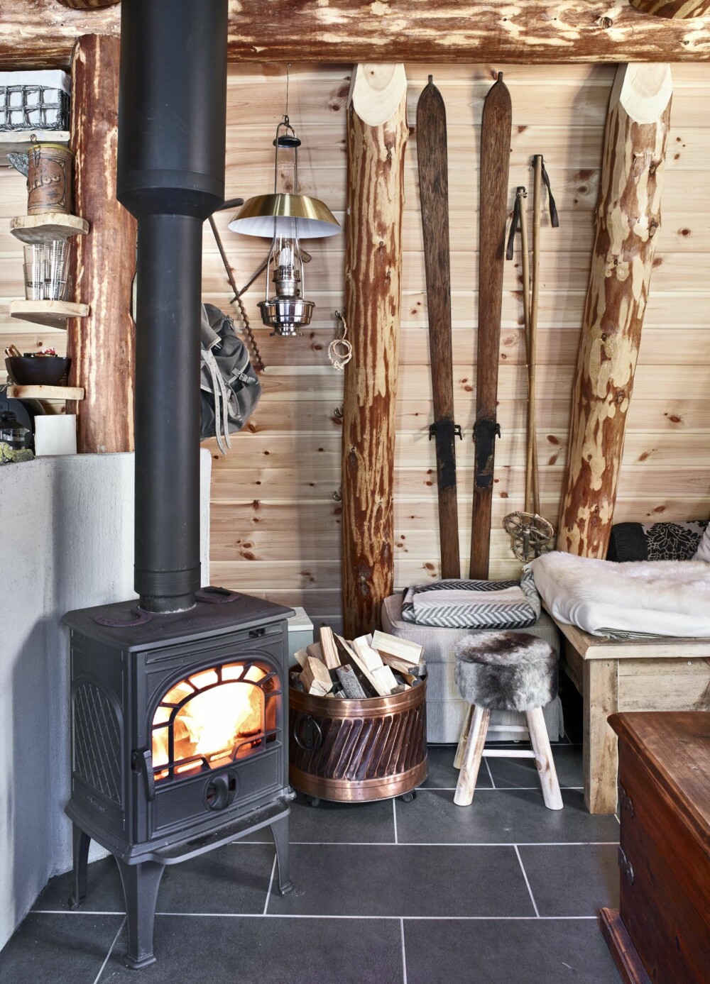 LUNT MED VEDOVN: Det tar ikke lang tid å få varme i hytta, som er godt isolert med jord og torv. Gamle ski og Ludvik-sekk bidrar til den nostalgiske interiørstilen. FOTO: Sveinung Bråthen 