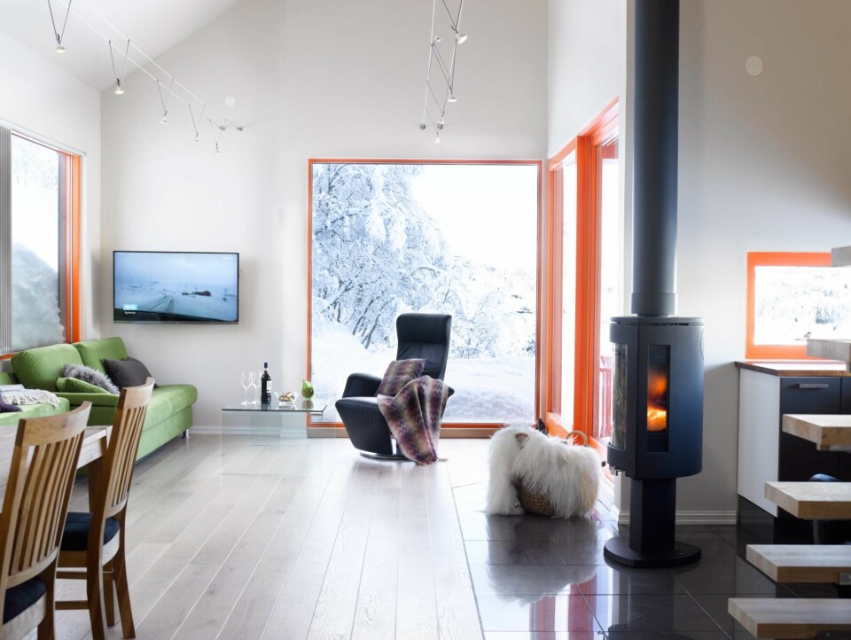 NATURLIG NÆRHET: Når man går inn i stuen i denne hytta, oppnås umiddelbar kontakt med naturen utenfor. Oransje karmer sørger for å fremheve og ramme inn det. Eierne har valgt en frisk fargekombinasjon av grønt og oransje i interiøret. Fliser er trukket gjennom stuen fra terrassedøren til entreen, så det er mulig å gå gjennom hytta med skoene på, uten å skade parketten. Peisen kan vris rundt.