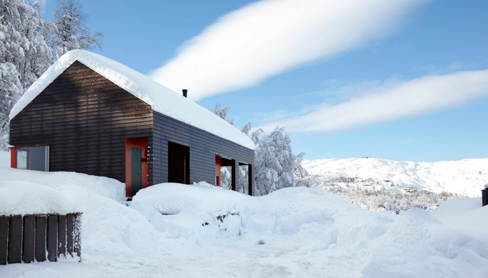 FINE KONTRASTER: Mot den blå himmelen og alt det hvite fremmes detaljene på denne hytta ekstra godt. Formen er stram og minimalistisk, men byggestilen er tradisjonell, og under snøen er det torvtak.
