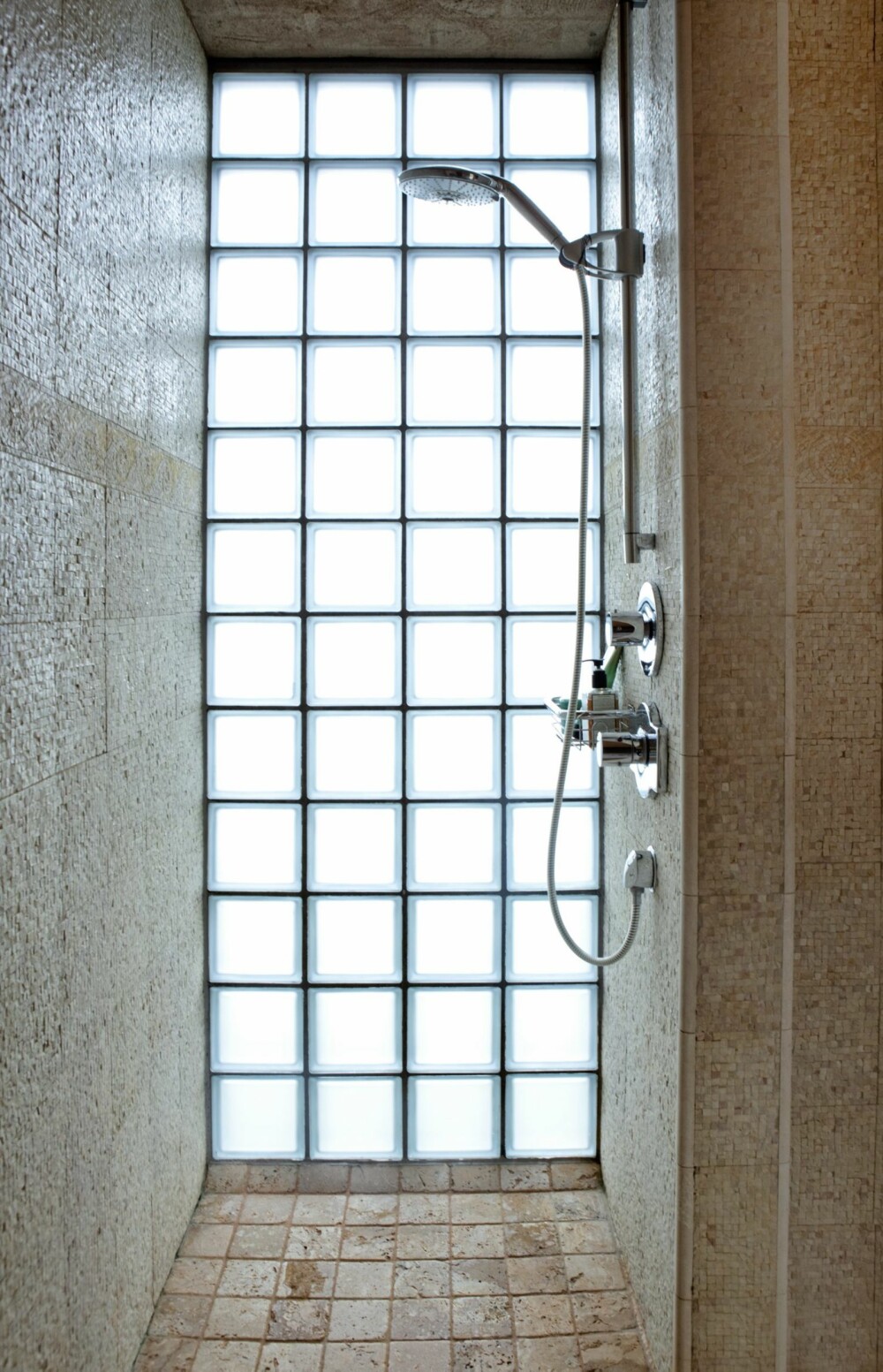 LYS I NISJER: Også i badeværelset får dagslyset spille hovedrollen. Her ser du hvordan deler ytterveggen er laget av glassbyggestein. Rustikke gulvfliser av toskansk travertin.