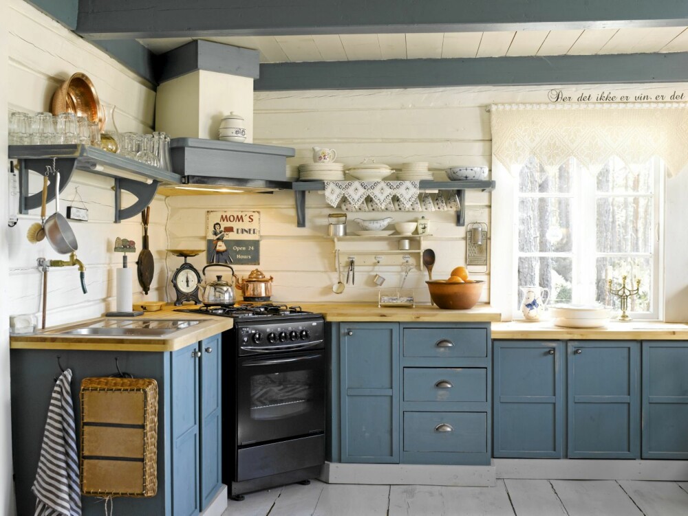 SELVLAGET: Det nydelige, blå kjøkkenet er det Arne som har bygget. Den smarte hjørneløsningen med ovnen var hytteeiernes egen idé. Det gamle skiltet har Hilde kjøpt i en interiørforretning i Arendal. Kobberkjelen tilhørte Arnes tippoldeforeldre, og stammer fra tidlig 1800 tallet.