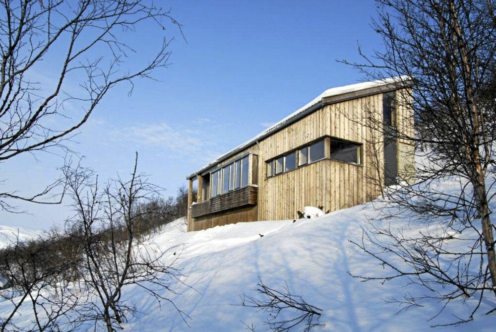 GRANKLEDD. Hytta ligger i en bratt skråning. På baksiden er det betong som tar i mot tung snø, mens fremsiden er kledd med gran.