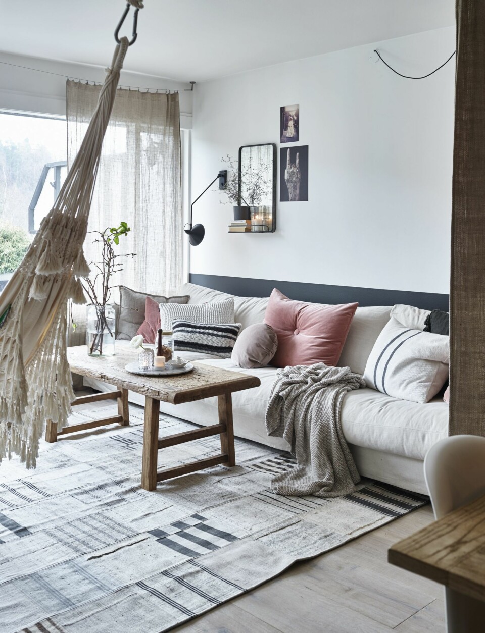 STUA TIL AINA: Bordet som står her nå, står vanligvis langs veggen, for i stuen er det turning og lek som gjelder. Sofa Heaven fra Skeidar, puter fra Verket Interiør og gulvteppe fra carpetvista.no. Hengekøya er stor nok til å romme hele familien. – Den stripete puten fortjener ekstra oppmerksomhet, den ble til under en hyggelig skravlekveld, og er heklet av min gode venninne Janne. Speilet på veggen og den svarte lampen er fra henholdsvis Home & Cottage og House Doctor. Bord fra Bloomingville. Fargen på veggen heter Elegant, fra Jotun. Resten av leiligheten er malt i helhvit 0500.