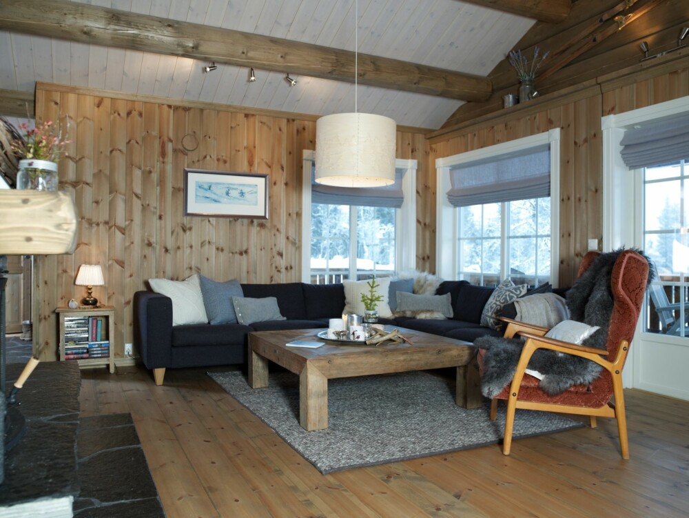 FORM OG FARGE: Sarah har valgt lysegrå lingardiner med stoff fra Home and Cottage til samtlige vinduer. Fargen tas fint opp i pynteputene i sofaen. Det store, kvadratiske bordet står godt til sofaens form. Det rustikke treverket går igjen i spisebordet og på peisstokken. Sofaen og bordet er fra Skeidar, stolen er arv fra Sarahs mormor. Lampen over bordet, Norwegian Forest, er designet av Cathrine Kullberg. Den er laget av tynn never med utskårne figurer og passer godt på fjellet. Hyttekroppen har et utbygd midtparti som rommer stuen. Her er saltaket trukket ut, slik at det danner en overbygget terrasse. (FOTO: Inger Mette Meling Kostveit) FORM OG FARGE: Sarah har valgt lysegrå lingardiner med stoff fra Home and Cottage til samtlige vinduer. Fargen tas fint opp i pynteputene i sofaen. Det store, kvadratiske bordet står godt til sofaens form. Det rustikke treverket går igjen i spisebordet og på peisstokken. Sofaen og bordet er fra Skeidar, stolen er arv fra Sarahs mormor. Lampen over bordet, Norwegian Forest, er designet av Cathrine Kullberg. Den er laget av tynn never med utskårne figurer og passer godt på fjellet. Hyttekroppen har et utbygd midtparti som rommer stuen. Her er saltaket trukket ut, slik at det danner en overbygget terrasse. (FOTO: Inger Mette Meling Kostveit)