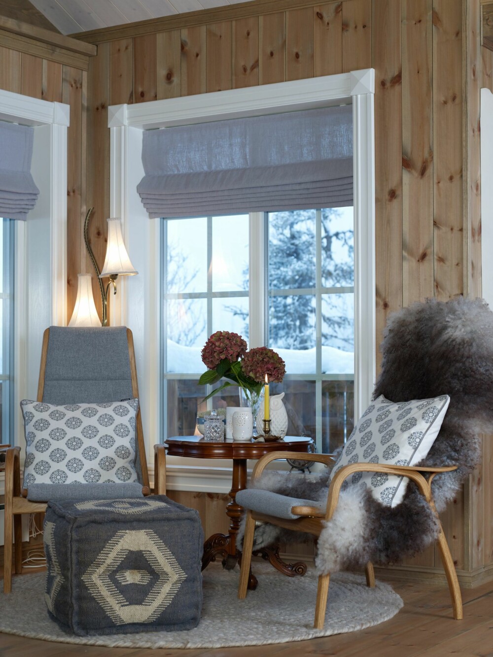 FAVORITTSTED: Lesekroken ved vinduet er Sarahs favorittplass. Den er møblert med to av de stilrene stolene Lamino fra Swedese, design Yngve Ekstrøm, trukket i et grått ullstoff. Bak dem står en særegen lampe, som er arvet etter Sarahs mormor. Puffen er kjøpt på Kremmerhuset, gulvteppe og gardinstoff er fra Home & Cottage. De mange skinnfellene i hytta er kjøpt på Oppland Bygg og Anleggs interiørutsalg. Det runde søylebordet er arvet. (FOTO: Inger Mette Meling Kostveit) FAVORITTSTED: Lesekroken ved vinduet er Sarahs favorittplass. Den er møblert med to av de stilrene stolene Lamino fra Swedese, design Yngve Ekstrøm, trukket i et grått ullstoff. Bak dem står en særegen lampe, som er arvet etter Sarahs mormor. Puffen er kjøpt på Kremmerhuset, gulvteppe og gardinstoff er fra Home & Cottage. De mange skinnfellene i hytta er kjøpt på Oppland Bygg og Anleggs interiørutsalg. Det runde søylebordet er arvet. (FOTO: Inger Mette Meling Kostveit)