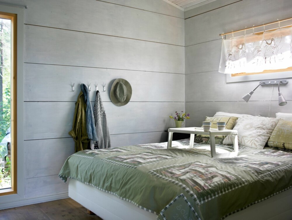 GRØNNE TEKSTILER: De massive veggene er holdt enkle og rene, med kun knagger med klær som dekor. De naturgrønne fargene i sengeteppe og puter står i fin stil til resten av rommet og skaper en rolig atmosfære.