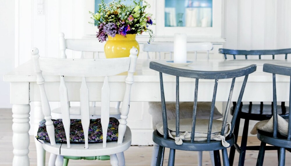 TREND I INTERIØRET: Spisestuen er lys og luftig med hvite vegger og tak, og et lyst tregulv. Både vitrineskapet og spisebordet går i ett med det hvite rommet. Beboerne har heller valgt å tilføre fargene i detaljene. Det blå glasset i vitrineskapet tar opp fargen fra de blå kjøkkenstolene, og en gul vase med fargerike blomster er plassert på bordet.