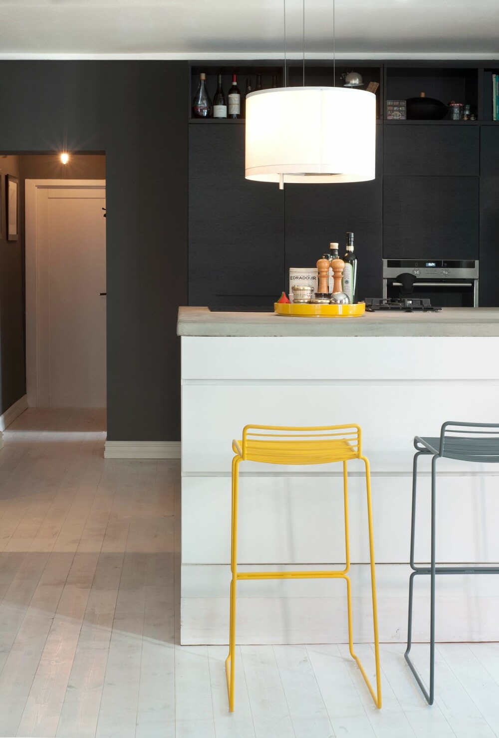 SVART, HVITT OG GULT: Kjøkkenveggen fra er kullsvart, mens kjøkkenøya er kritthvit. Dermed får den gule barkrakkene fra Hay en utpreget signaleffekt. Benkeplaten i slipt mur er 250 cm bred og 140 cm dyp. Over koketoppen henger en kombinert lampe/avtrekkshette fra Ikea.
Innredningen er fra Kvik.