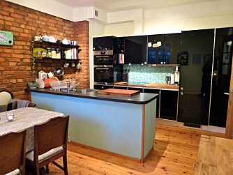 Den moderne kjøkkeninnredningen i sort og blåtoner står i kontrast til den rustikke murveggen.
