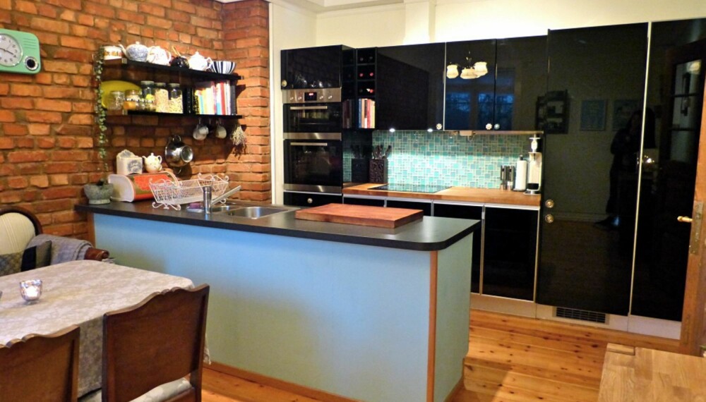 Den moderne kjøkkeninnredningen i sort og blåtoner står i kontrast til den rustikke murveggen.