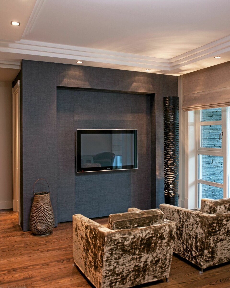 MATT TV-VEGG. Satser du på svart matt, går fjernsynet mer i ett med veggen. Bildet er tatt hjemme hos interiørdesigner Lone Schrøder Haagensen. Langs gulvet har veggen en skyggekant med list i børstet stål, dette får veggen til å 'sveve'. Tapet Madagascar VP 631-31.