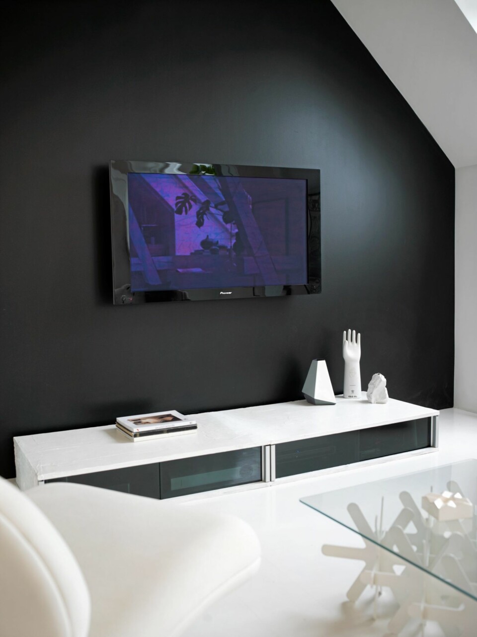 SVART MAGI. Den enkleste og kanskje rimeligste måten å dempe tv-flaten på, er å male veggen svart bak. Veggen er også fin kontrast til hvite vegger. Tv-møblet er hjemmesnekret, de sotede skyvedørene skjuler nødvendig tilbehør uten å hindre signalene fra fjernkontrollen.