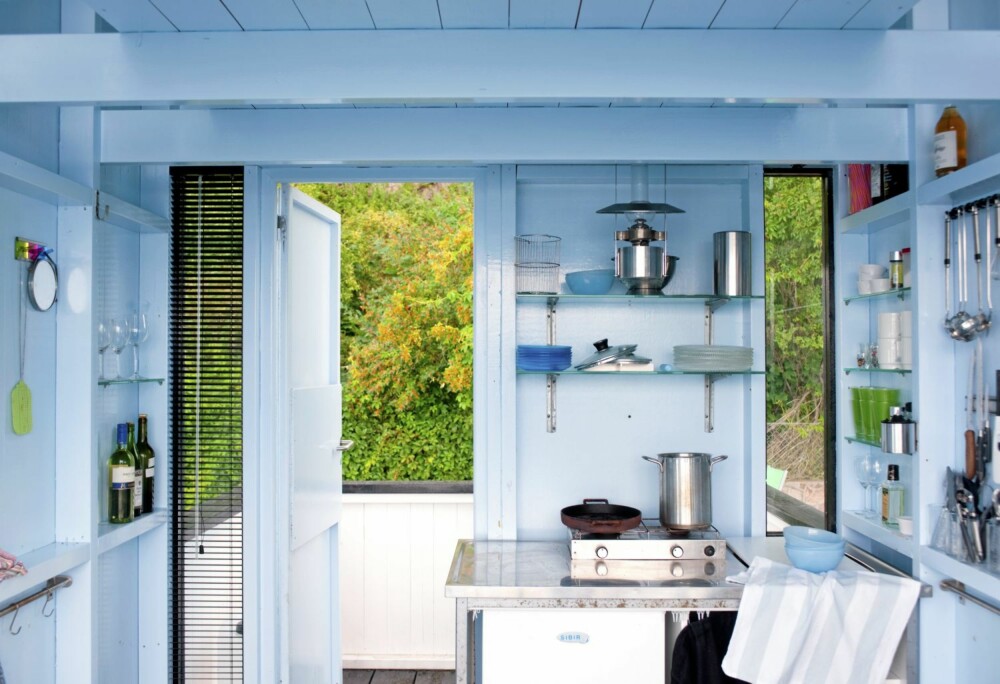 LYSEBLÅ DRØM. Kjøkkenet i dette badehuset er malt i blått, både tak, bjelker og vegger og døren ut til terrassen. Alt av kjøkkenutstyr er fullt tilgjengelig på veggene rundt.