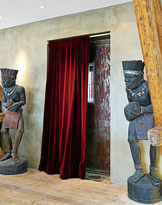 PÅ PLASS. To skulpturer fra Bali vokter vareheisen. Velurstoffet matcher rødfargen på døren.