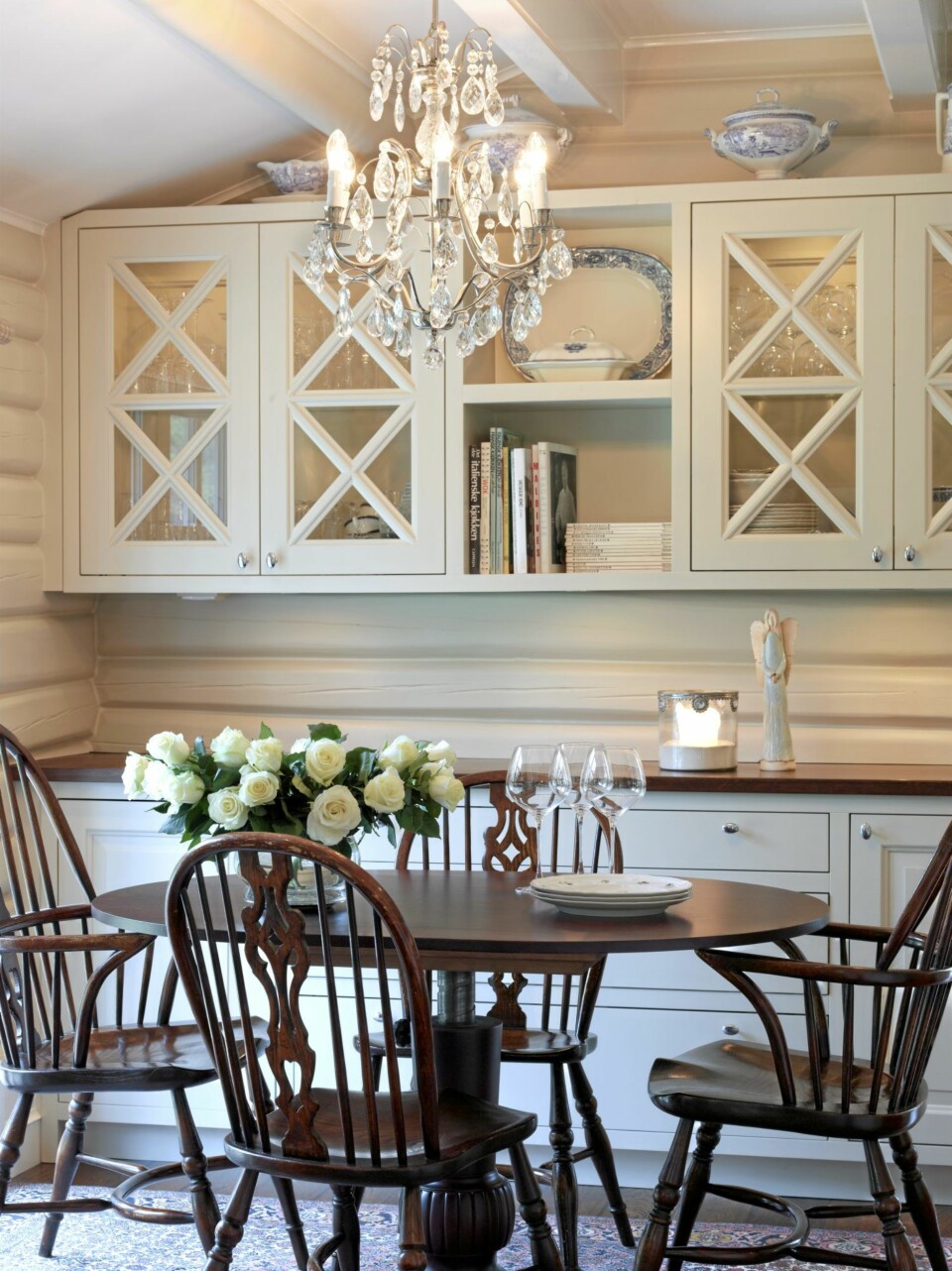 HVIT DRØMMESTUE. I spisestuen har tømmerveggene blitt malt i naturhvit, slik at de går i ett med innredningen. Det rødbrune spisebordet med tilhørende trestoler tar opp fargen fra benkeplaten, og demper den ellers så lyse innredningen. Veggene er malt med S1505-Y20R. Stolene er fra Delford House.