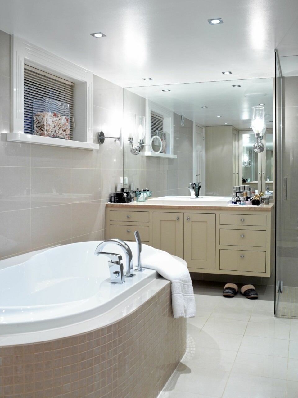 LYST BAD. Badet preges av duse farger, både på fliser og på baderomsmøblementet. Tak, vinduslister og gulvflisene er derimot holdt i hvitt. Det ovale badekaret er omringet av beige mosaikk, og i vinduskarmen står en glasskrukke med koraller fra Maldivene.