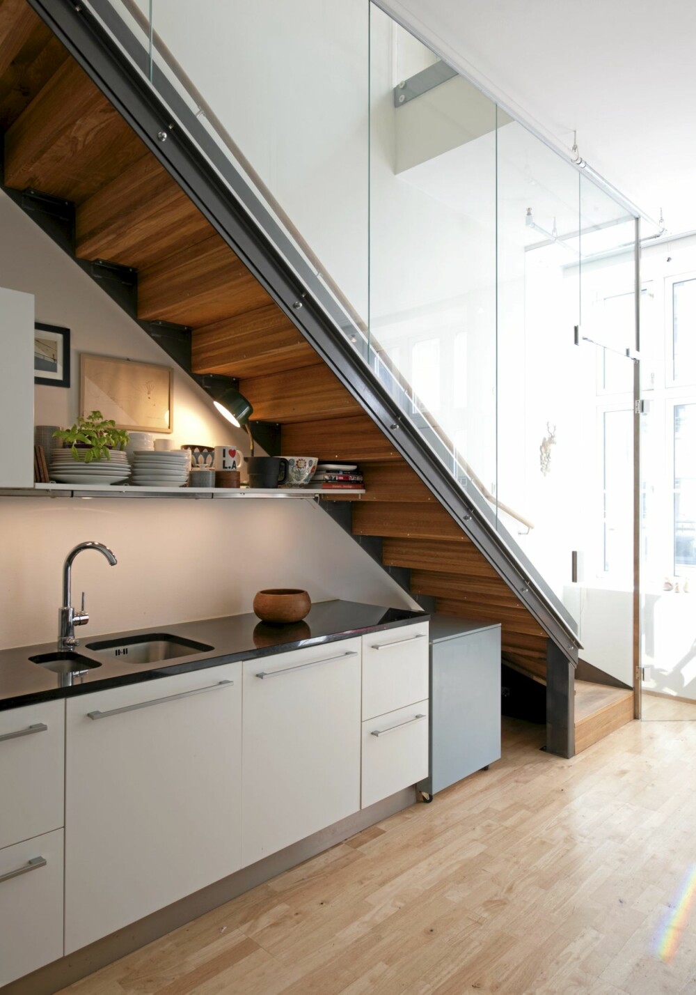 KJØKKENBENK UNDER TRAPPA: Undersiden av den tette trappen er i oljet tre, og utgjør en dekorativ innramming av kjøkkenet. Glassveggen sørger for å gi siktlinjer mellom første- og annenetasjen.