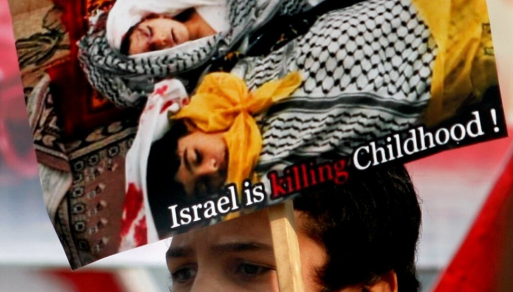 TUNGT: En palestinsk tenåring demonstrerer mot de israelske angrepene på Gaza med en plakat som viser tre barnelik. Bildene fra krigen på Gazastripen er råere enn dem vi har sett før.