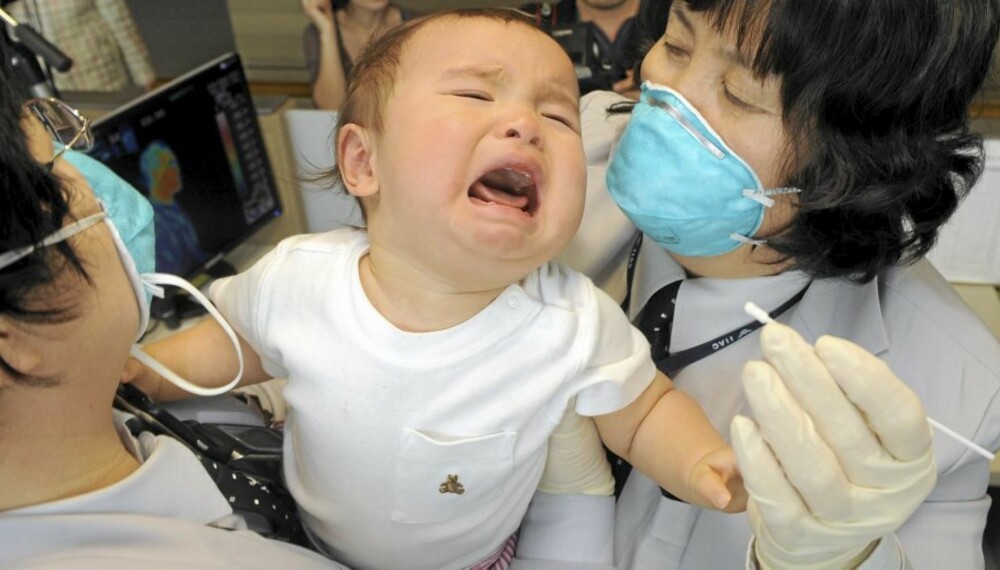 TESTES FOR INFLUENSA: Sør-Koreansk helsepersonell forsøker å ta en prøve av en baby som har ankommet med fly fra USA.