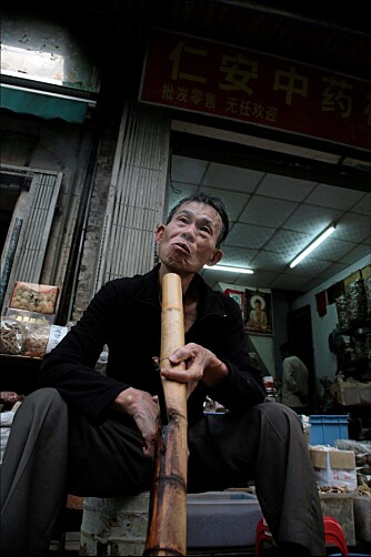 RØYKSTOKK: Yu Xi (70+) tilbringer store deler av dagen utenfor en medisinbutikk i Guangzhou mens han nyter dype drag av bambuspipen sin.