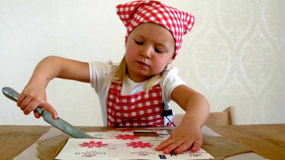 MAL AV MELKEKARTONG: Nora skjærer rundt kantene til en melkekartong. Denne har blitt brukt som mal til pepperkakehuset.