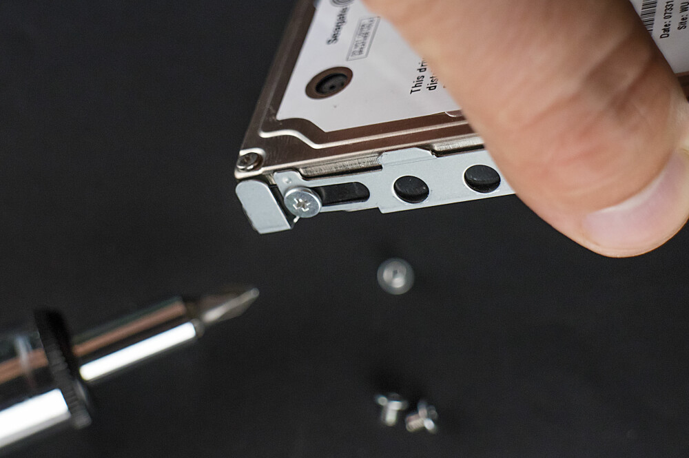 3. Selve harddisken er skrudd fast i en metallholder. Skru løs de fire skruene i hvert hjørne for å løsne den. 