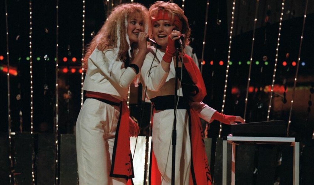 DOLLIE DE LUXE (1984): Dollie-duoen Ingrid Bjørnov og Benedicte Adrian stakk av med seieren med låta «Lenge leve livet», og vi glemmer ikke sceneantrekket til Norges nye popyndlinger.  
I 1984 var det Karate Kid-feber, noe popduoen visste å utnytte til det fulle. Da de troppet opp på scenen i musikkonkurransen, var de iført hvite karatedrakter, med tjukke belter og høye hæler.