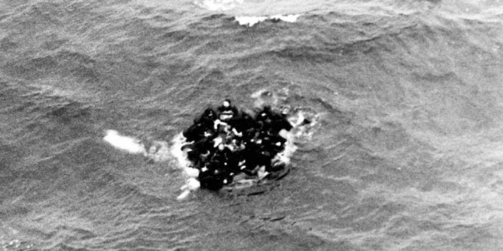 Besetningsmedlemmer klamrer seg fast i den ene flåten mens de venter på unnsetning. Den norske Orionbesetningen som tok bildet, hadde ikke med seg redningsutstyr som kunne spart flere liv. De fleste som omkom frøs i hjel i det to grader kalde vannet.