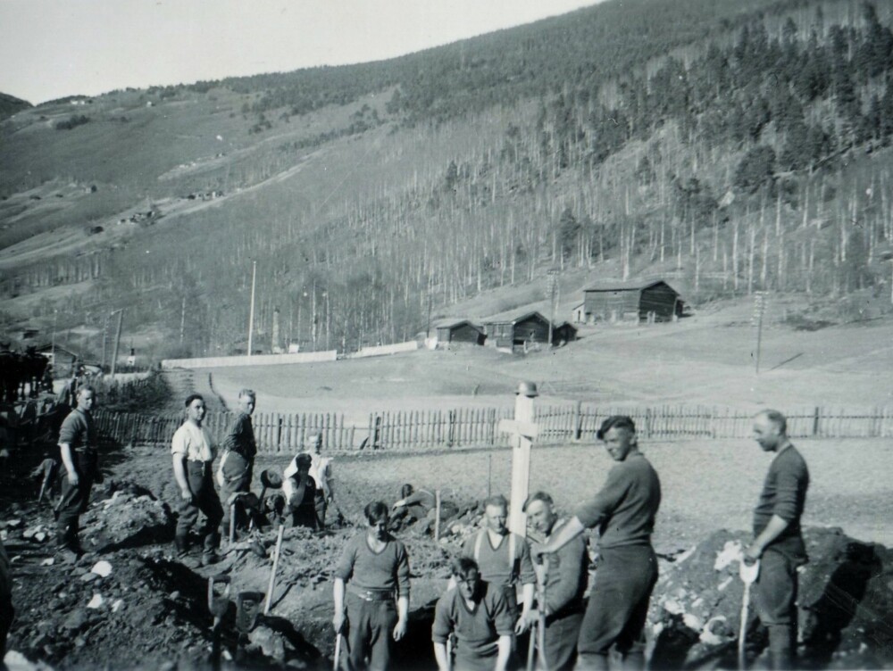 En tysk soldat fotograferer, mens britiske krigsfanger er satt til å spa opp graver. Bildet er tatt i nærheten av Otta.