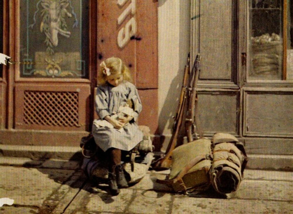 Reims, Frankrike, 1917: Dette fantastiske bildet viser ei jente og dukken hennes som tilsynelatende sitter helt uanfektet ved siden av en soldats sekk og våpen.