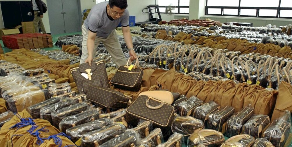 PIRATKOPIERTE VESKER: En politimann viser fram falske Louis Vuitton vesker som ble konfiskert under en rassia i Seoul i mai 2004.