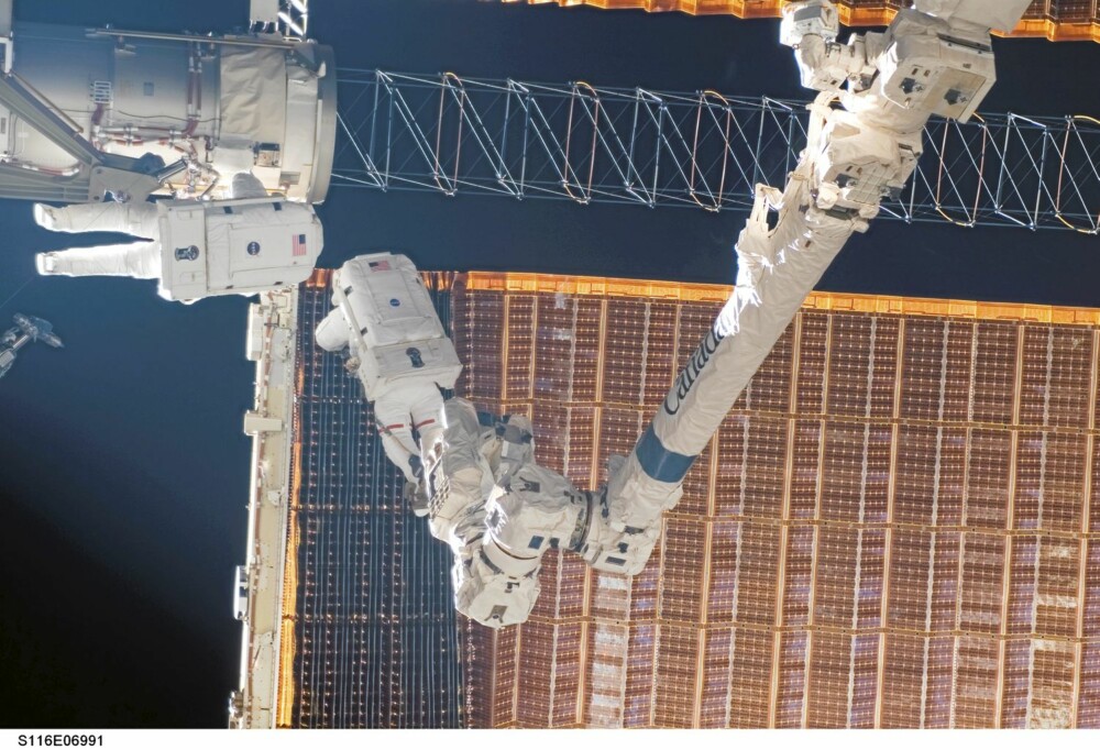 FØRSTE ARBEIDSØKT: Fuglesang (nærmest) og Curbeam i arbeid på det virkelige rammeverket mens romstasjonen svever ca. 350 km over New Zealand. Legg merke til det langsgående, brune rekkverket som astronautene benytter blant annet når de skal forflytte seg. De er hele tiden sikret med minst én line. Bildet er tatt under den første av Fuglesangs tre arbeidsøkter utenfor på STS-116 ferden.