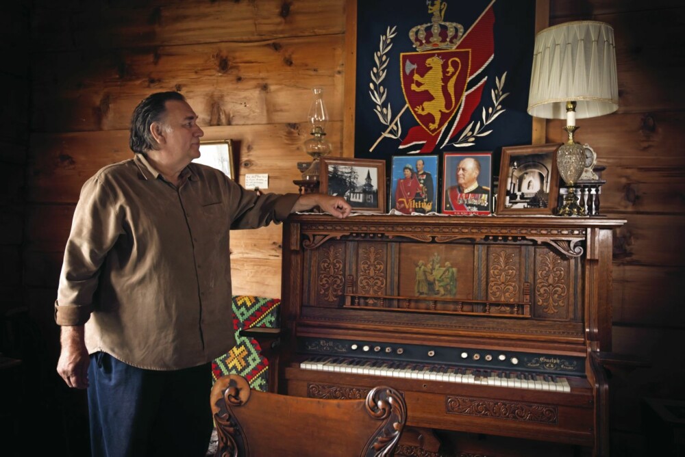 Peter Solhjell foran kongebilder og det norske flagget i det restaurerte hjemmet til den norske nybyggeren Andrew Svisdahl.