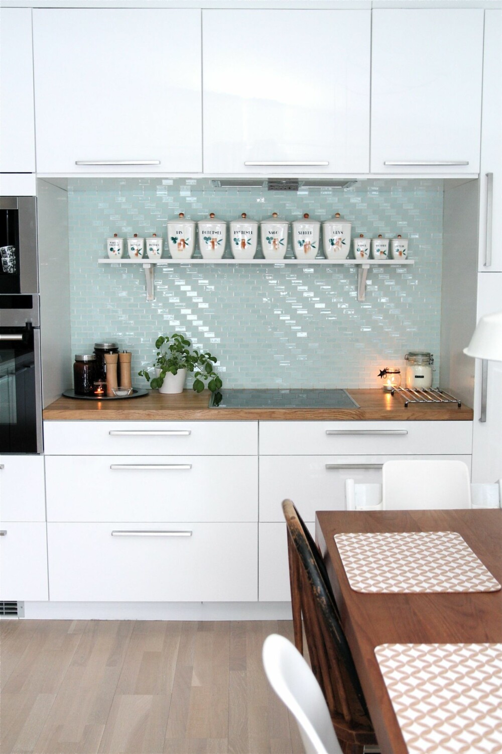 Kjøkken med moderne hvite fronter, lysblå glassmosaikk og nostalgiske detaljer.